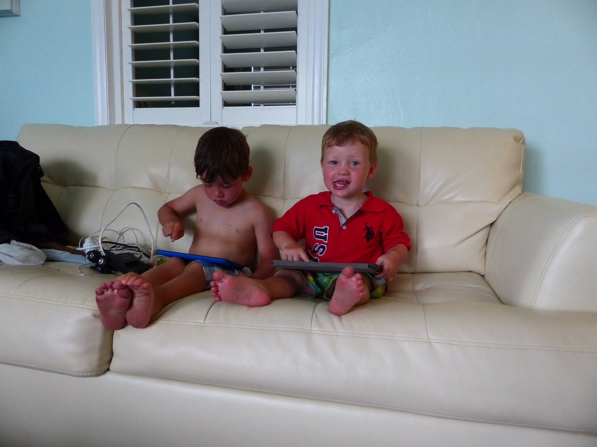 Noah and Vitus on the white leather couch in Miami — clean, happy, and blissfully unaware of the flight home
