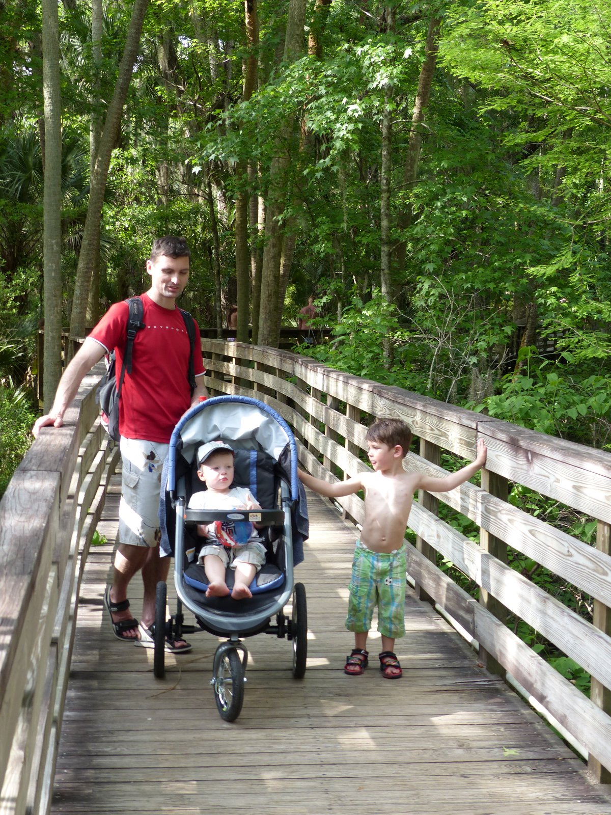Jesper pushing the stroller on a boardwalk through the forest with Noah walking beside him