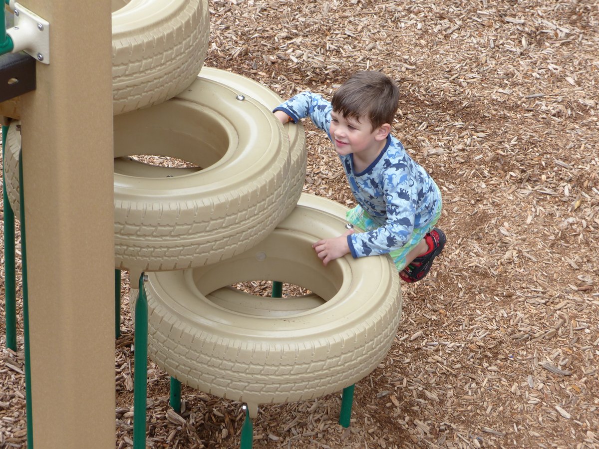 Noah climbing a tire structure at a playground — fearless and slightly worrying