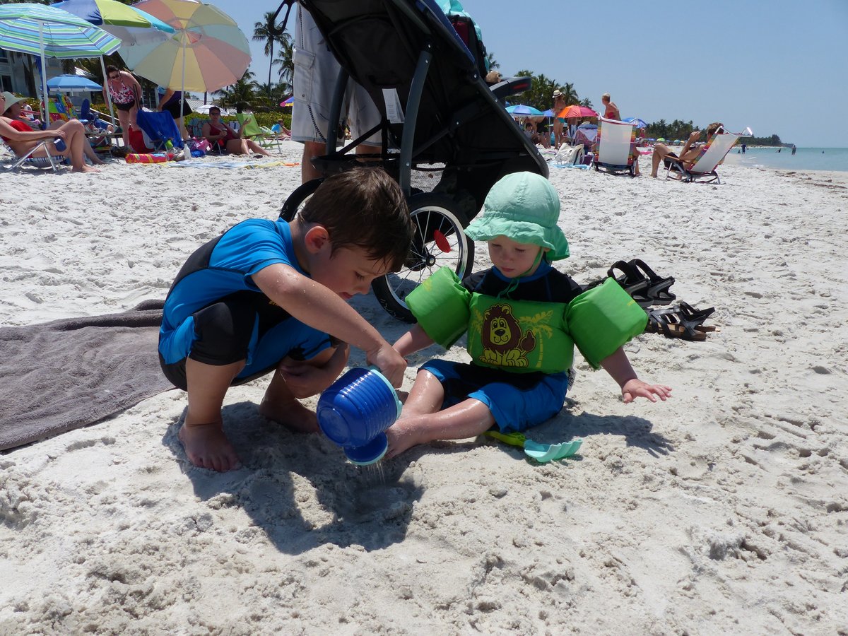 Both boys playing on the white sand beach — Noah in blue, Vitus in green with his bucket