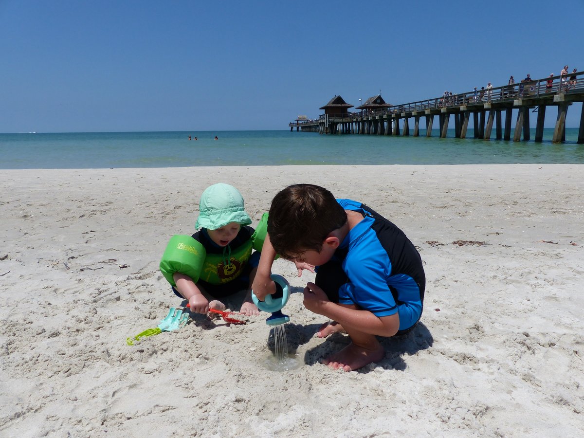 Both boys digging in the sand with Naples Pier clearly visible in the background