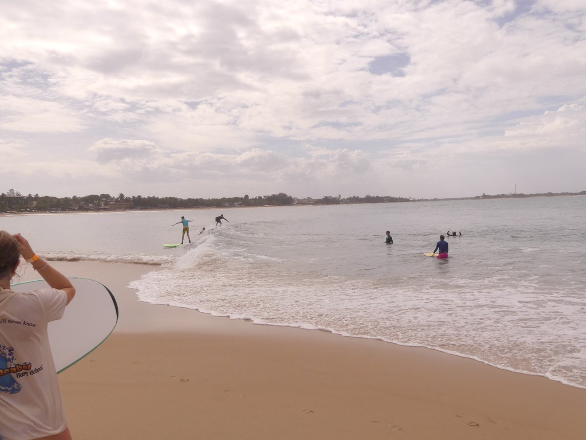 Vitus far out riding a wave, seen from the beach, in yellow shorts