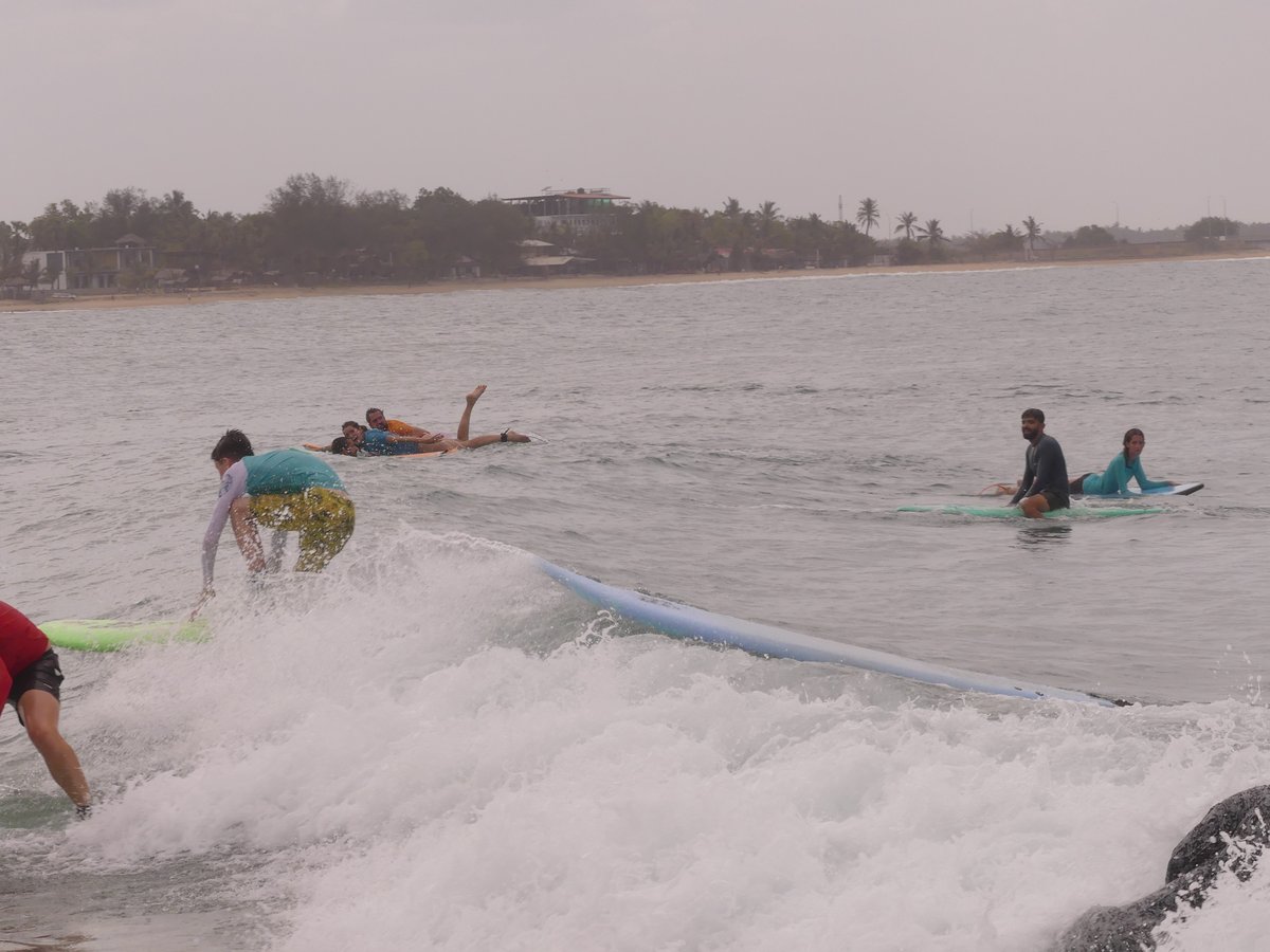 Vitus up on his board riding a whitewater wave with other surfers behind