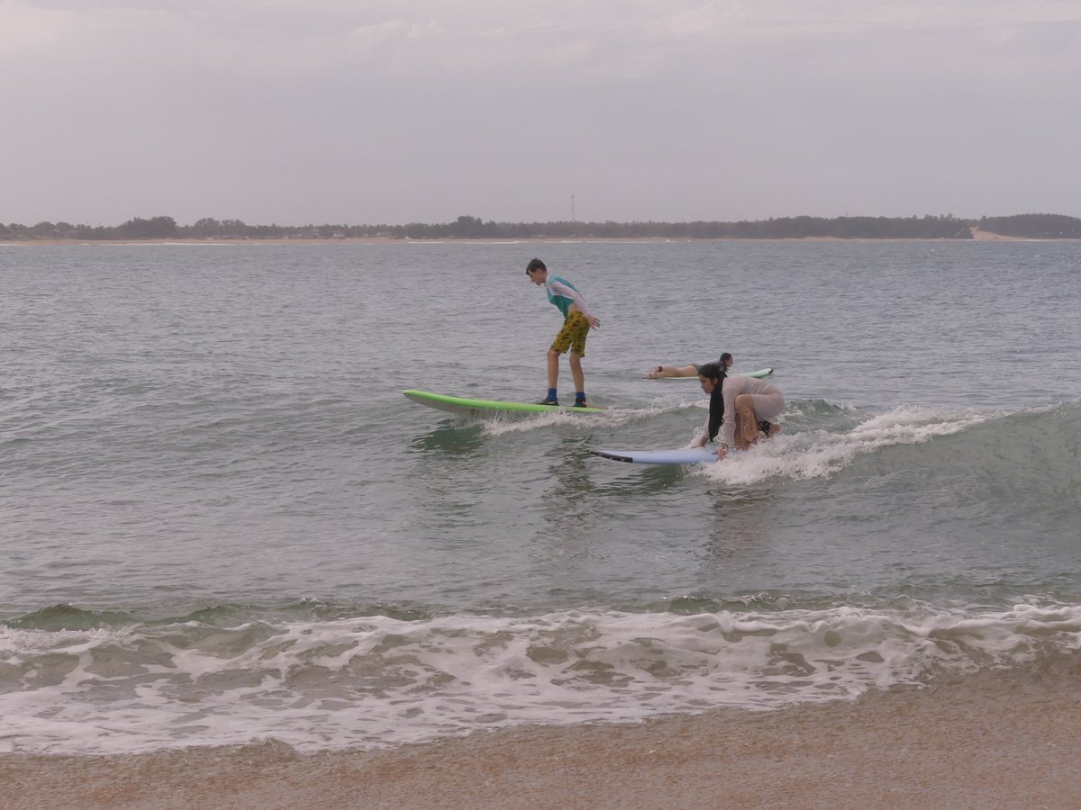 Vitus standing on his board riding a wave alongside an instructor