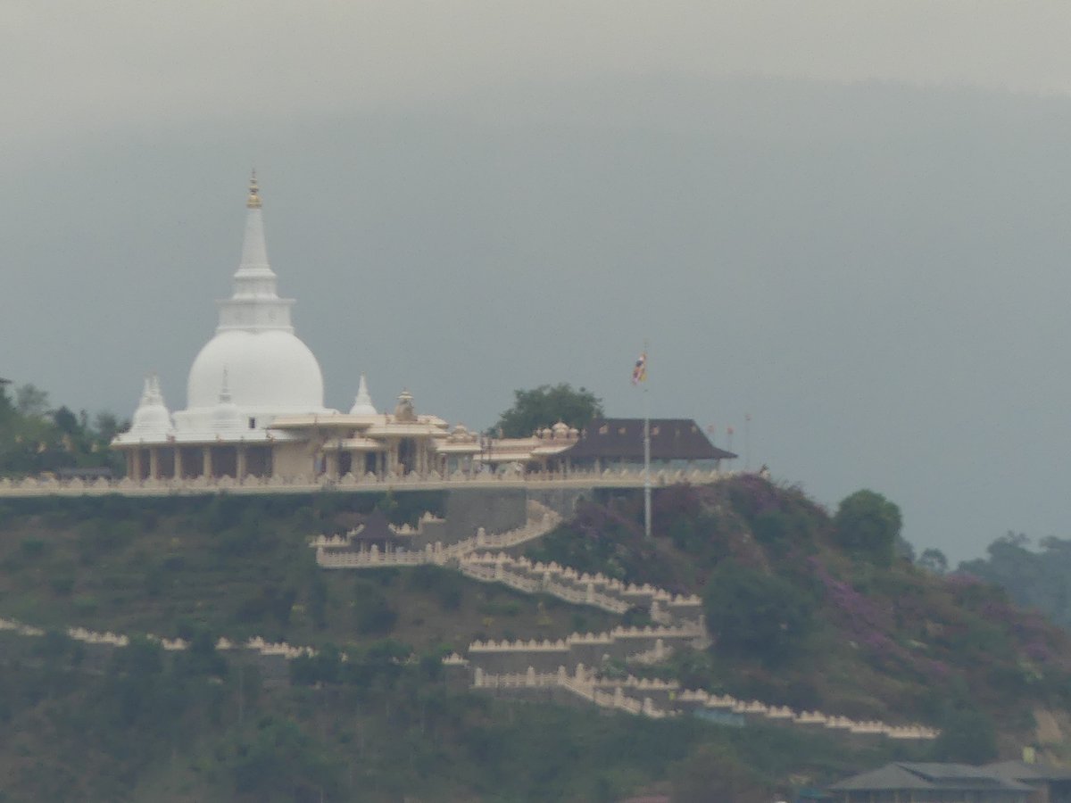 A white dagoba and temple complex on a distant hilltop seen from Little Adam's Peak
