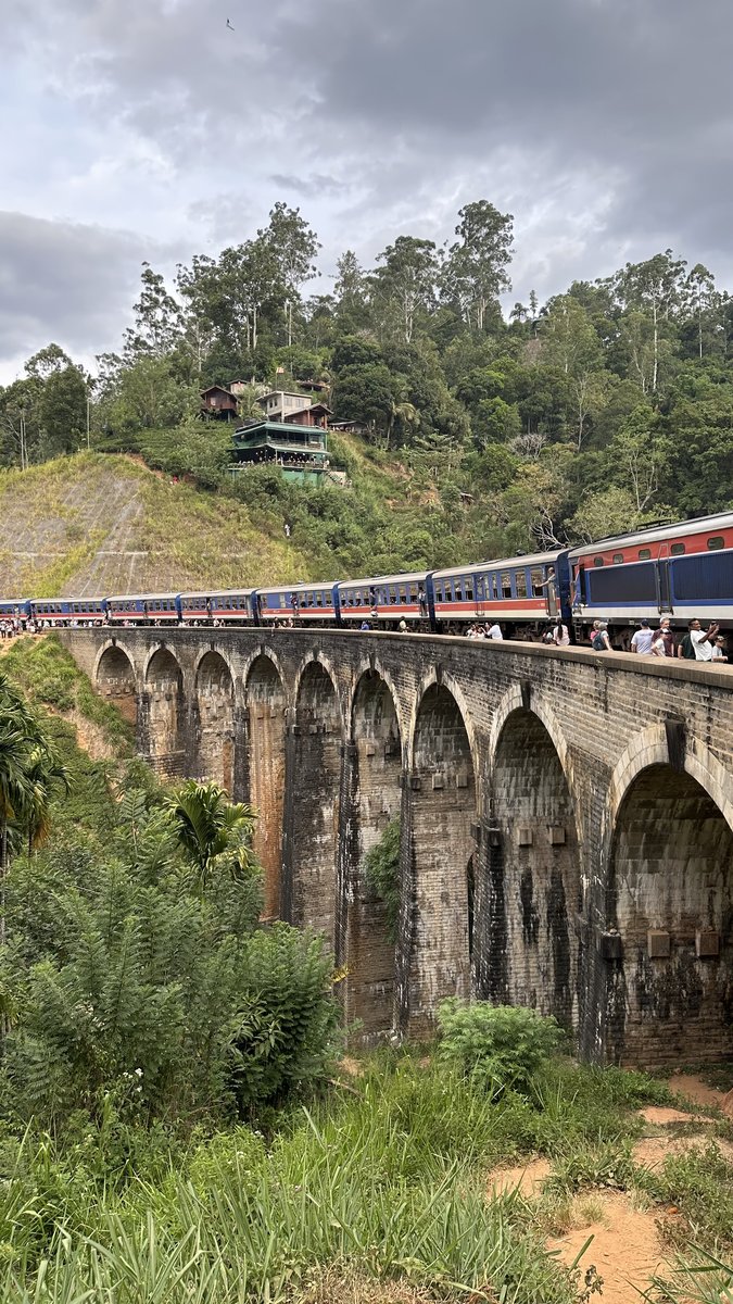 A train crossing the top of Nine Arches Bridge with people watching from the sides