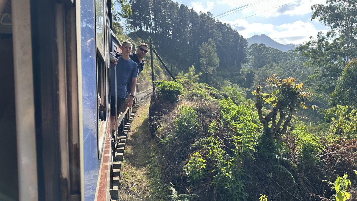 View from the train doorway over forested hills and the railway line ahead