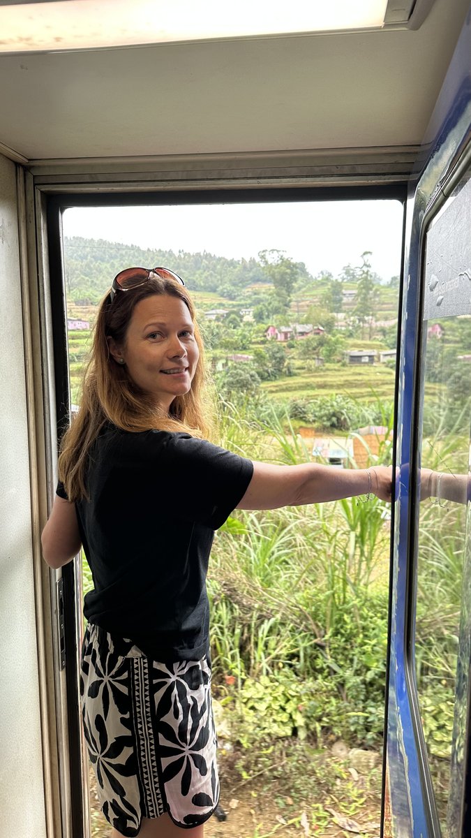 Line leaning out of the open train doorway with tea slopes and a village behind