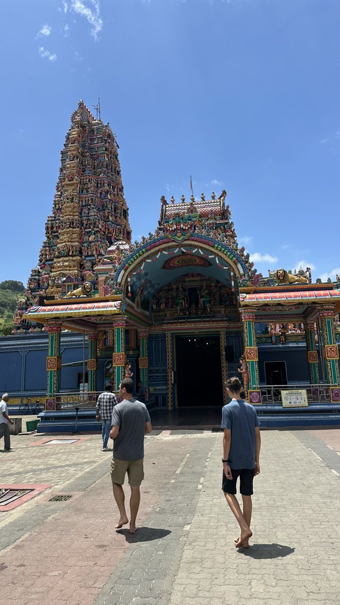Jesper and Noah walking barefoot toward a colourful Hindu temple with a figure-covered tower