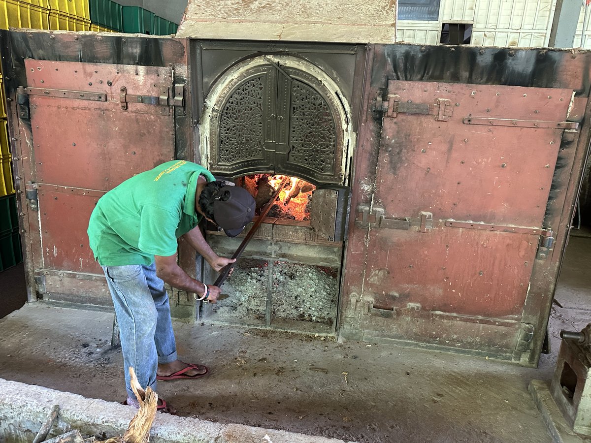 A worker tending the glowing wood-fired furnace that dries the tea