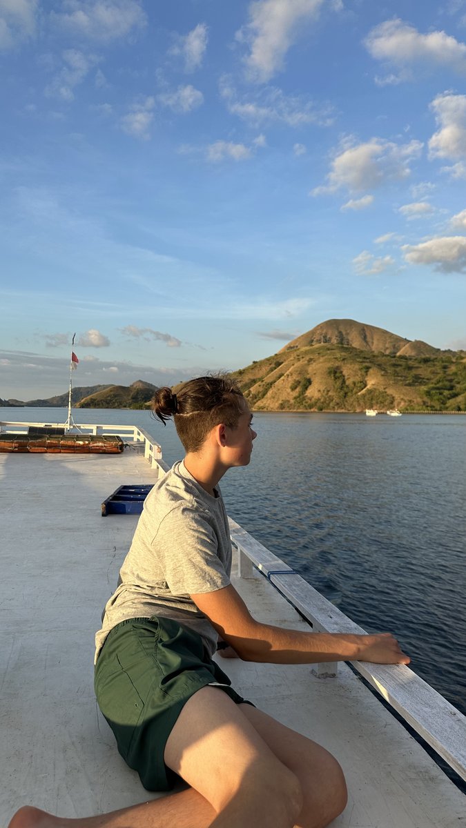 Noah looking out over the water from the boat deck, Komodo hills behind