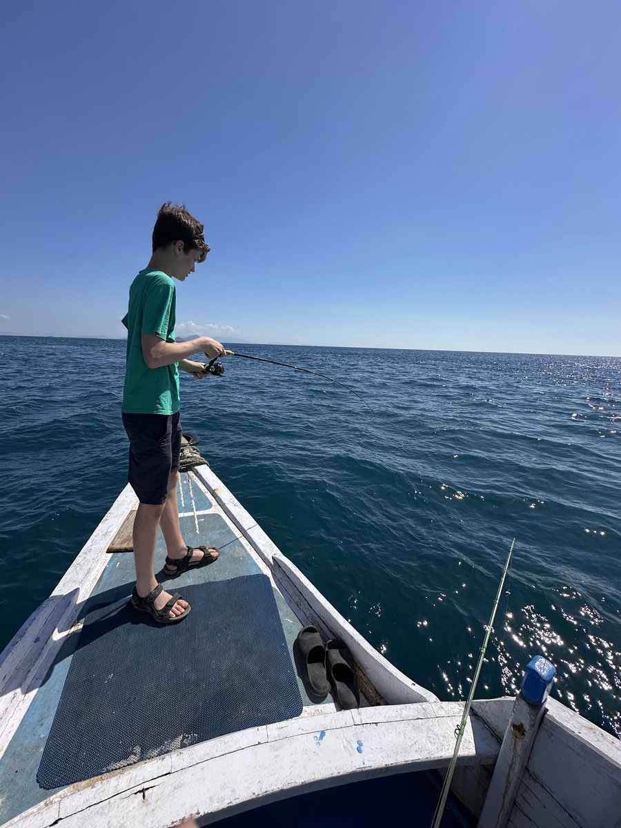 Noah on the bow of the old wooden boat with a fishing rod bent over the water