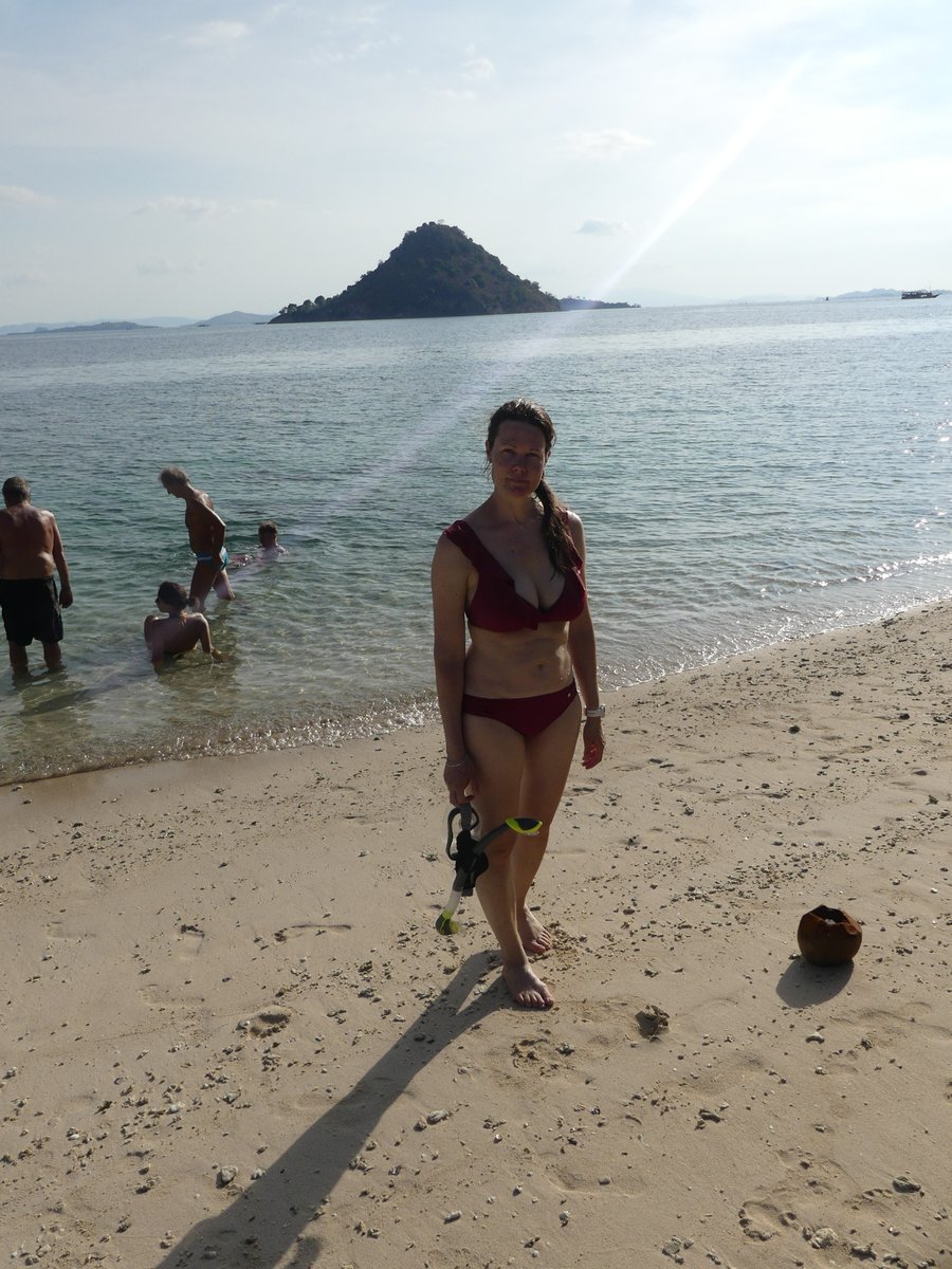 Line walking up the Kelor beach with snorkel gear, the cone-shaped island behind