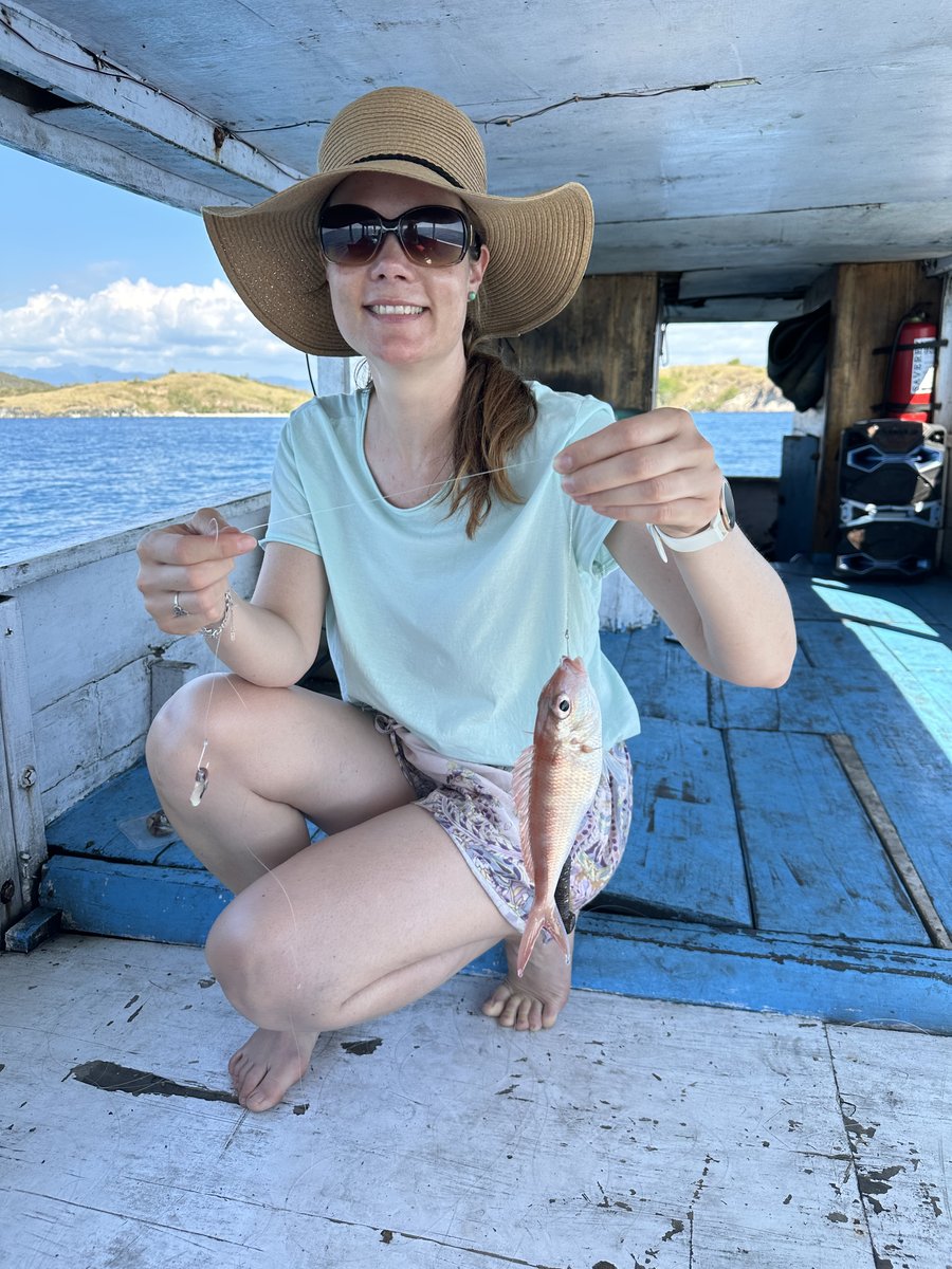Line in her sun hat crouched on the boat holding up a small pink fish