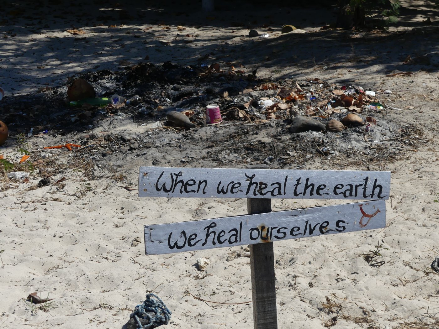 A hand-painted sign in the sand reading 'When we heal the earth, we heal ourselves'