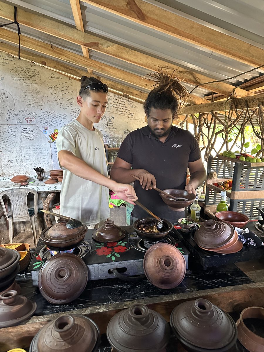 Noah cooking alongside Ishy at the row of clay curry pots