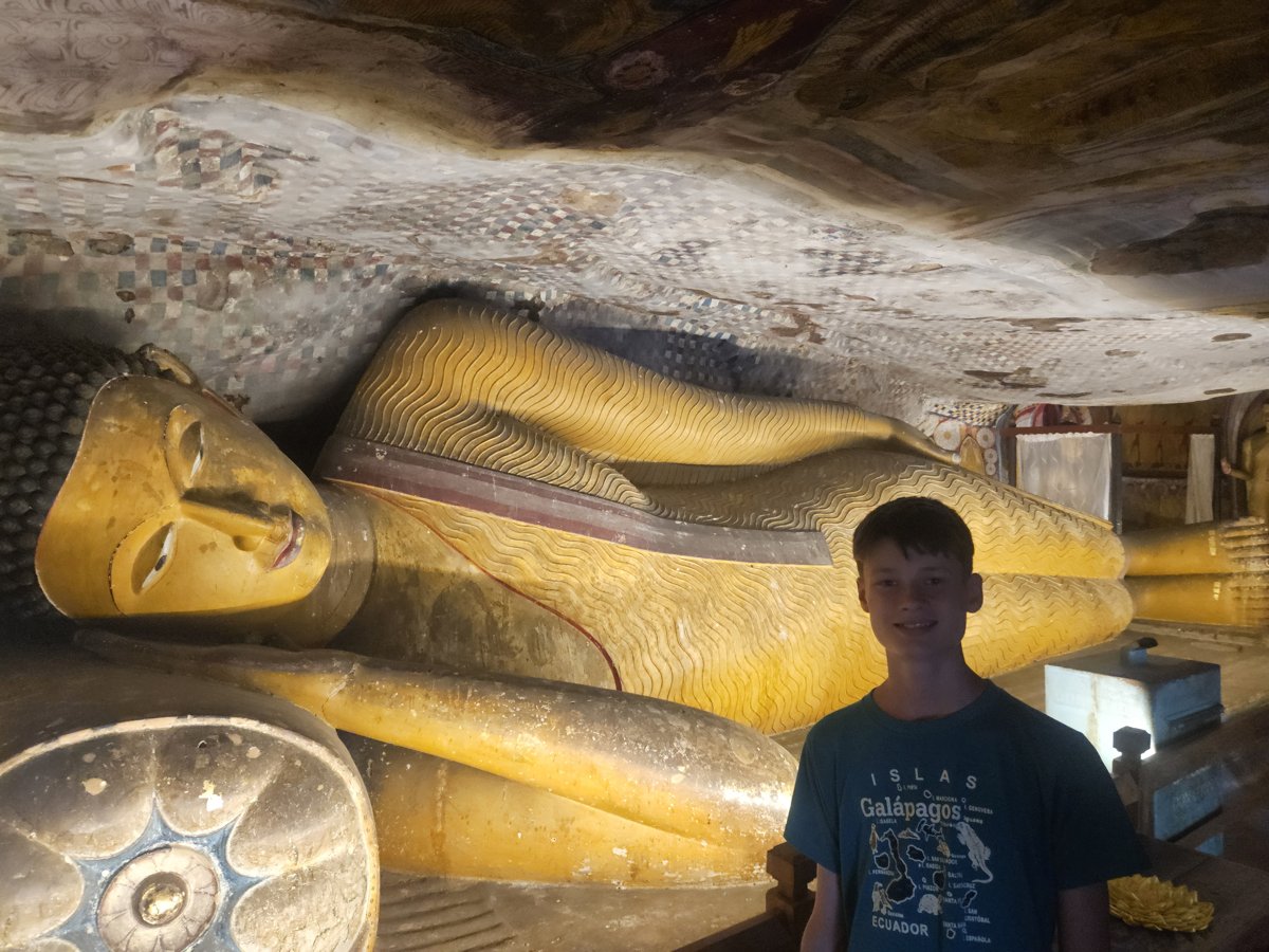 Noah beside a large gilded reclining Buddha inside a Dambulla cave