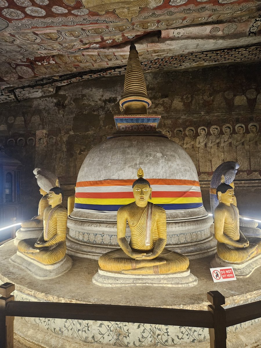 A stupa ringed with a Buddhist flag and gilded seated Buddhas under a painted rock ceiling