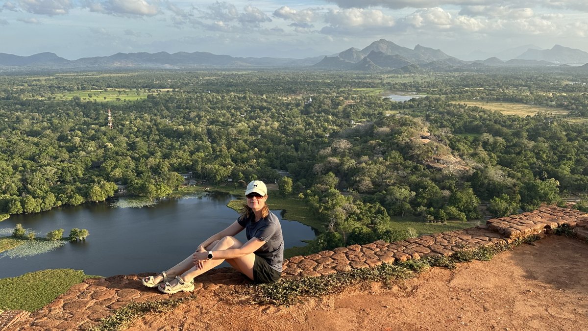 Line sitting on the summit edge with the jungle, water gardens and distant mountains behind