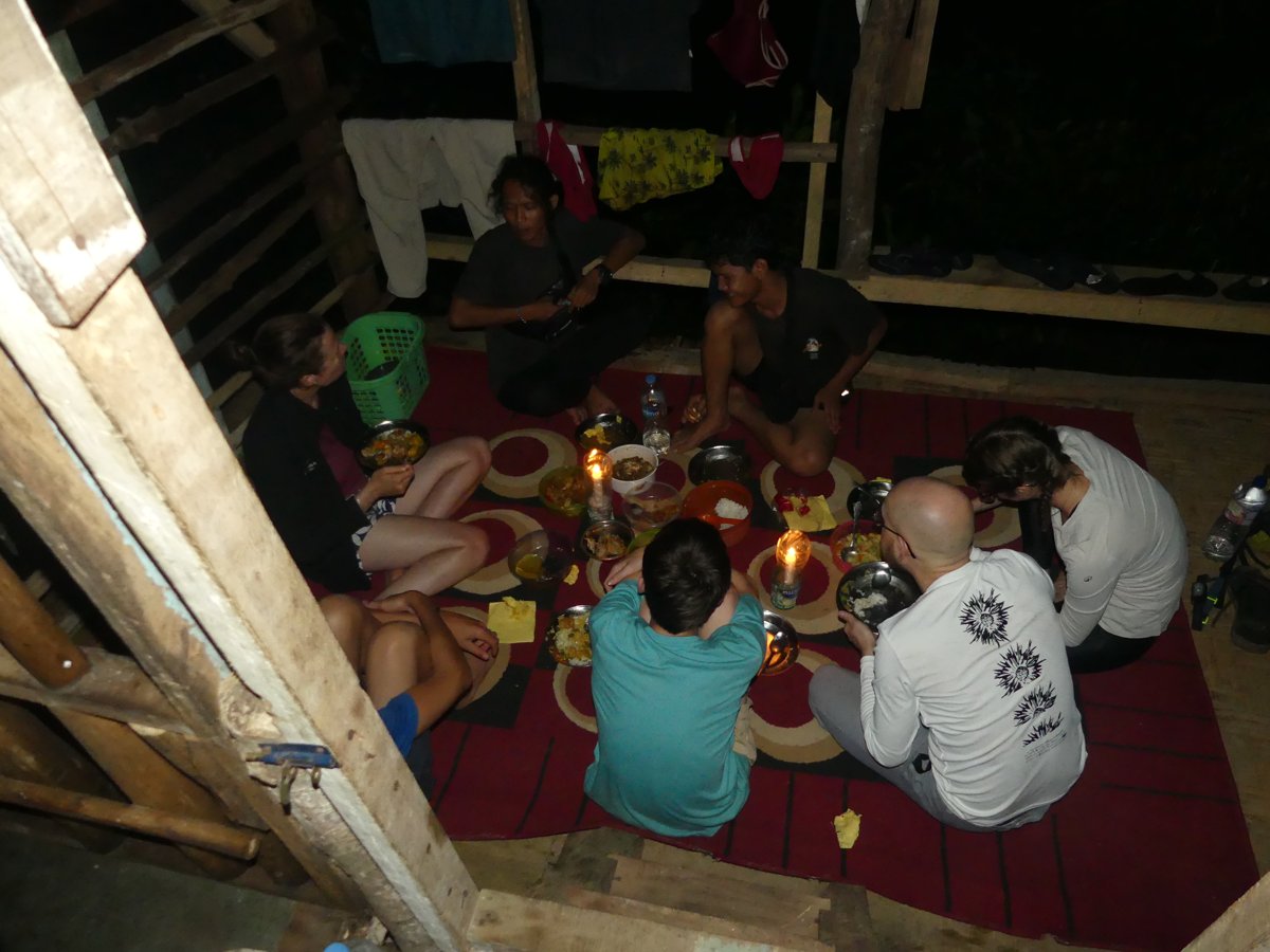 Everyone eating dinner together by candlelight on the floor of the hut